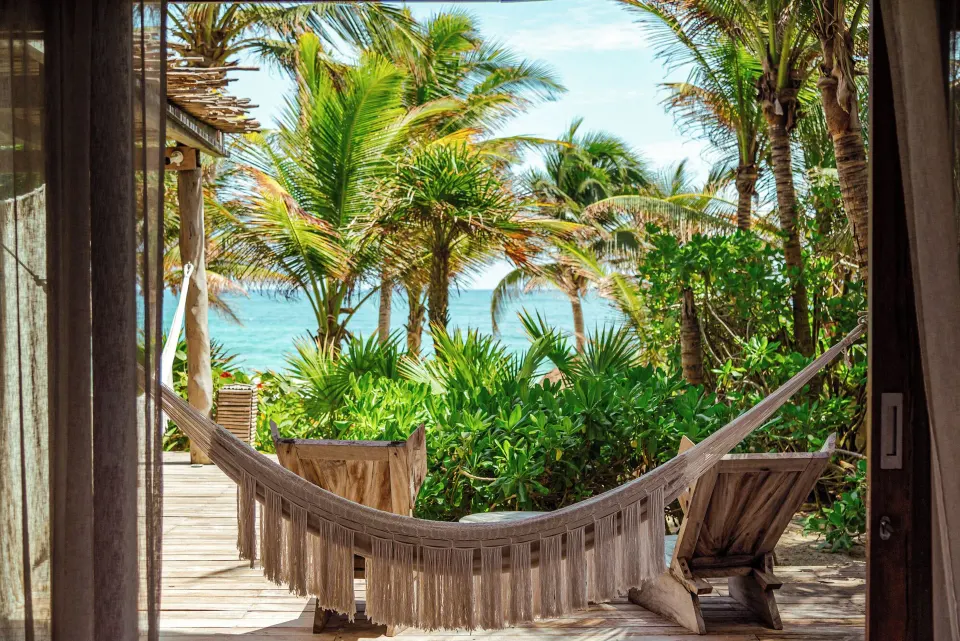 Fringed hammock and wooden chair on a deck framing ocean view at La Valise Tulum.