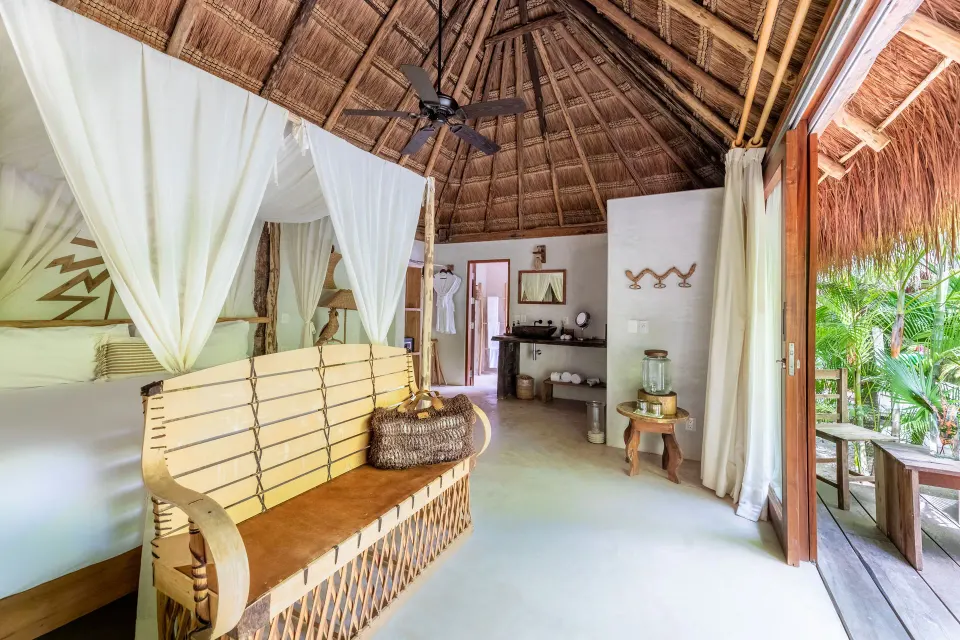 Interior view of a canopy king bed and wooden bench with open terrace at La Valise Tulum.