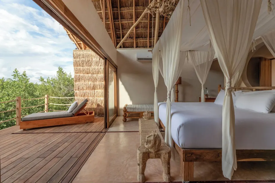Four-poster bed opening to a hardwood deck and lounger at La Valise Tulum.