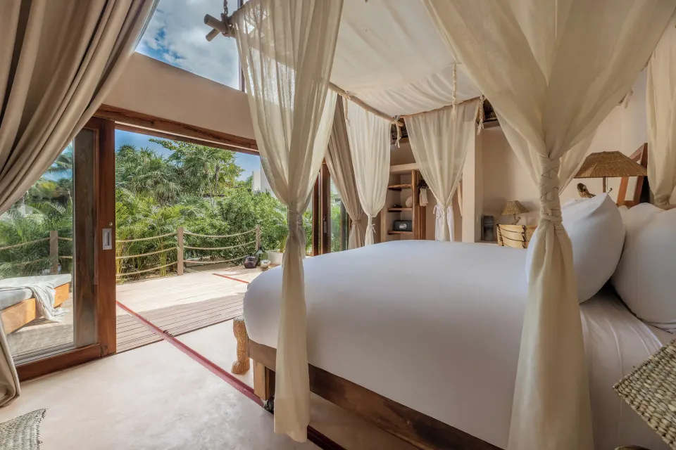 Canopy king bed opening onto a wooden terrace and tropical foliage at La Valise Tulum.
