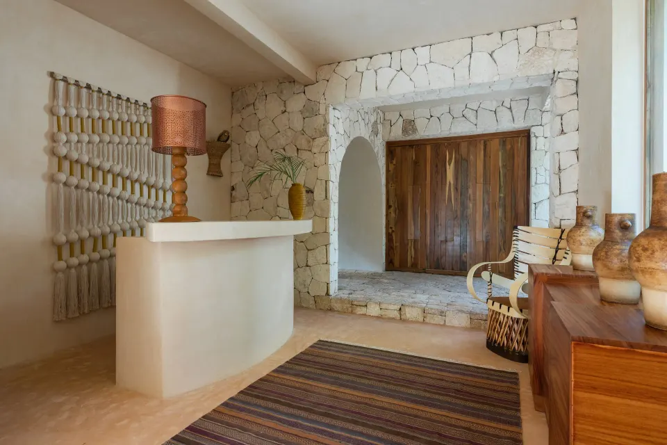 Lobby interior with wooden doors, woven rug and stone archway at La Valise Tulum.