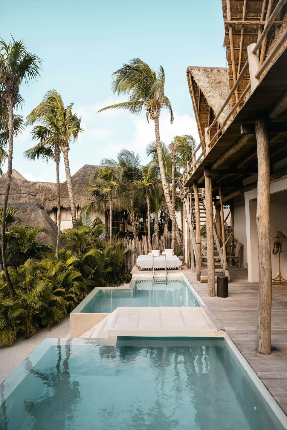 Row of plunge pools and sun beds along a deck under palm trees at La Valise Tulum