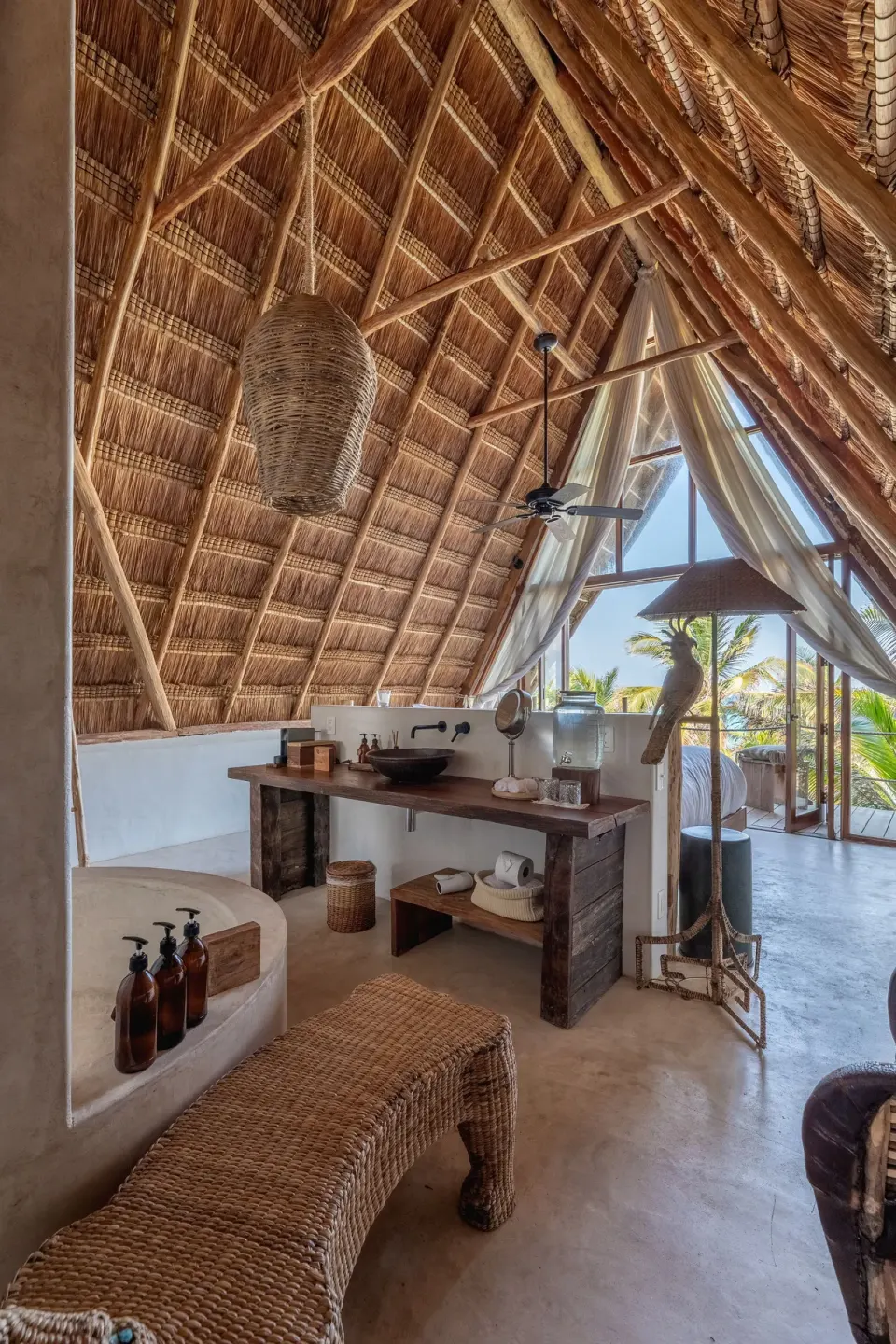 Open-air suite with high thatched ceiling, vanity and view to the outdoors at La Valise Tulum