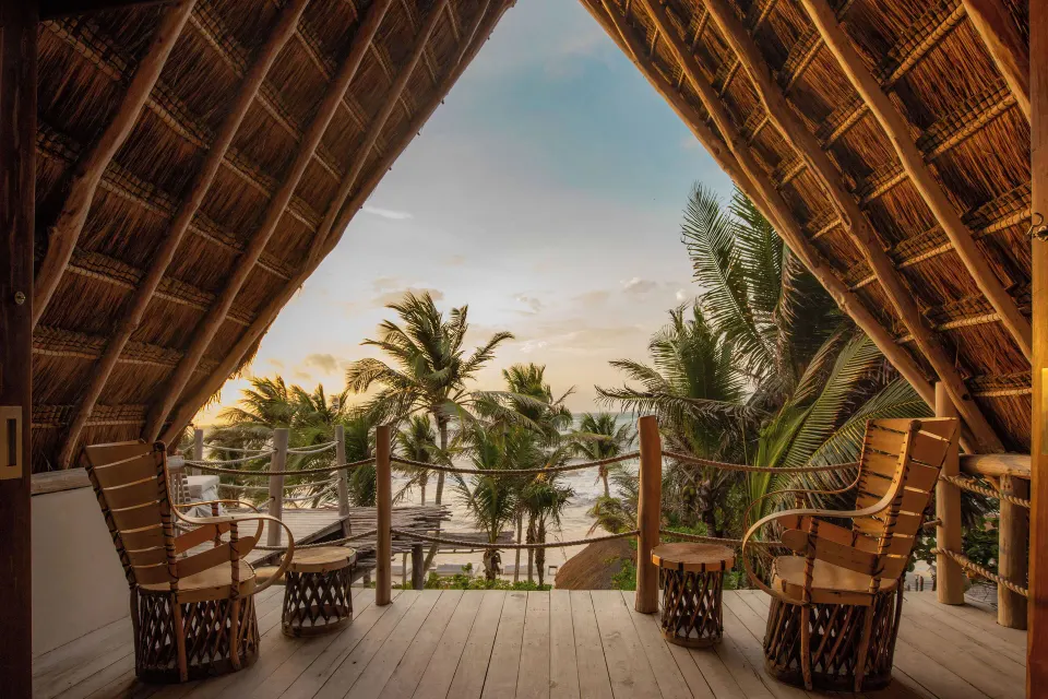 Thatched balcony with two chairs and ocean glimpses at La Valise Tulum.