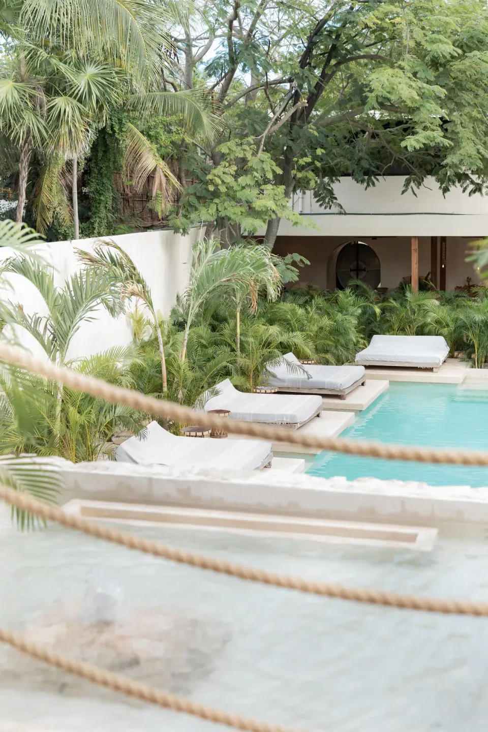 Resort pool with in-water loungers and cushioned beds surrounded by palms at La Valise Tulum.