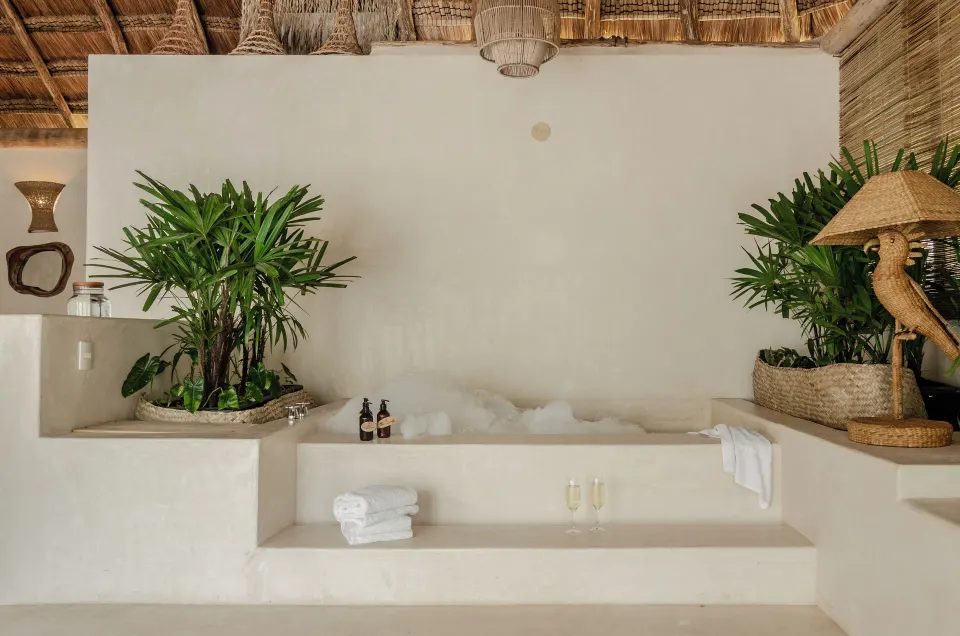 Built-in soaking tub with foam, tropical plants and thatched roof at La Valise Tulum