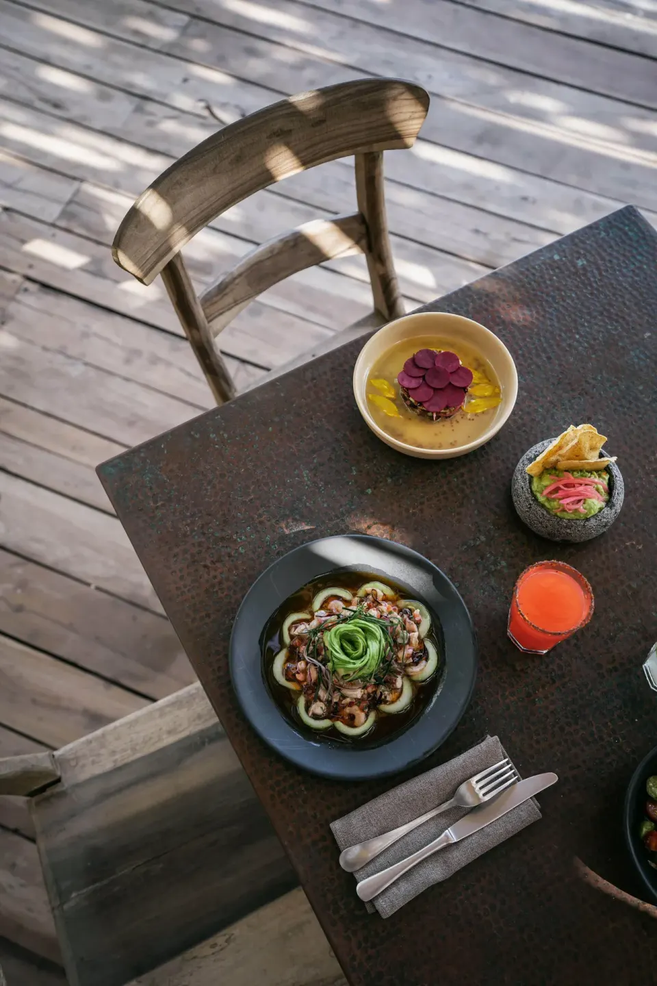 Table with plated appetizers and a drink on a wooden deck at La Valise Tulum