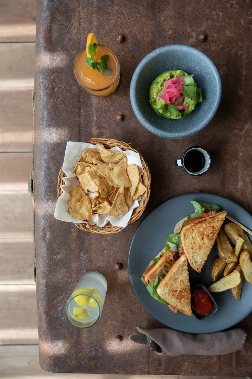 Table with sandwich, chips, guacamole and drinks on a rustic surface at La Valise Tulum