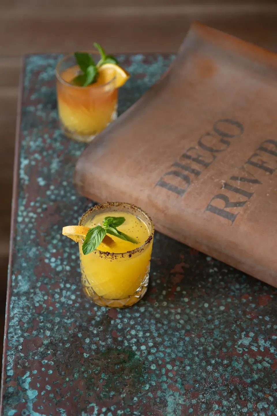 Two citrus cocktails beside a book on a weathered table at La Valise Tulum
