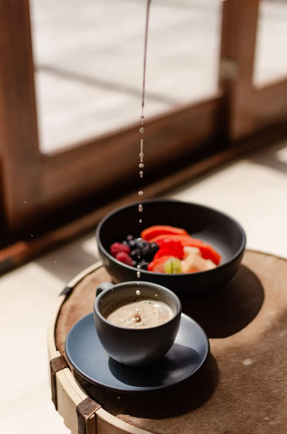 Coffee cup and fruit bowl on a small table with droplets falling above at La Valise Tulum