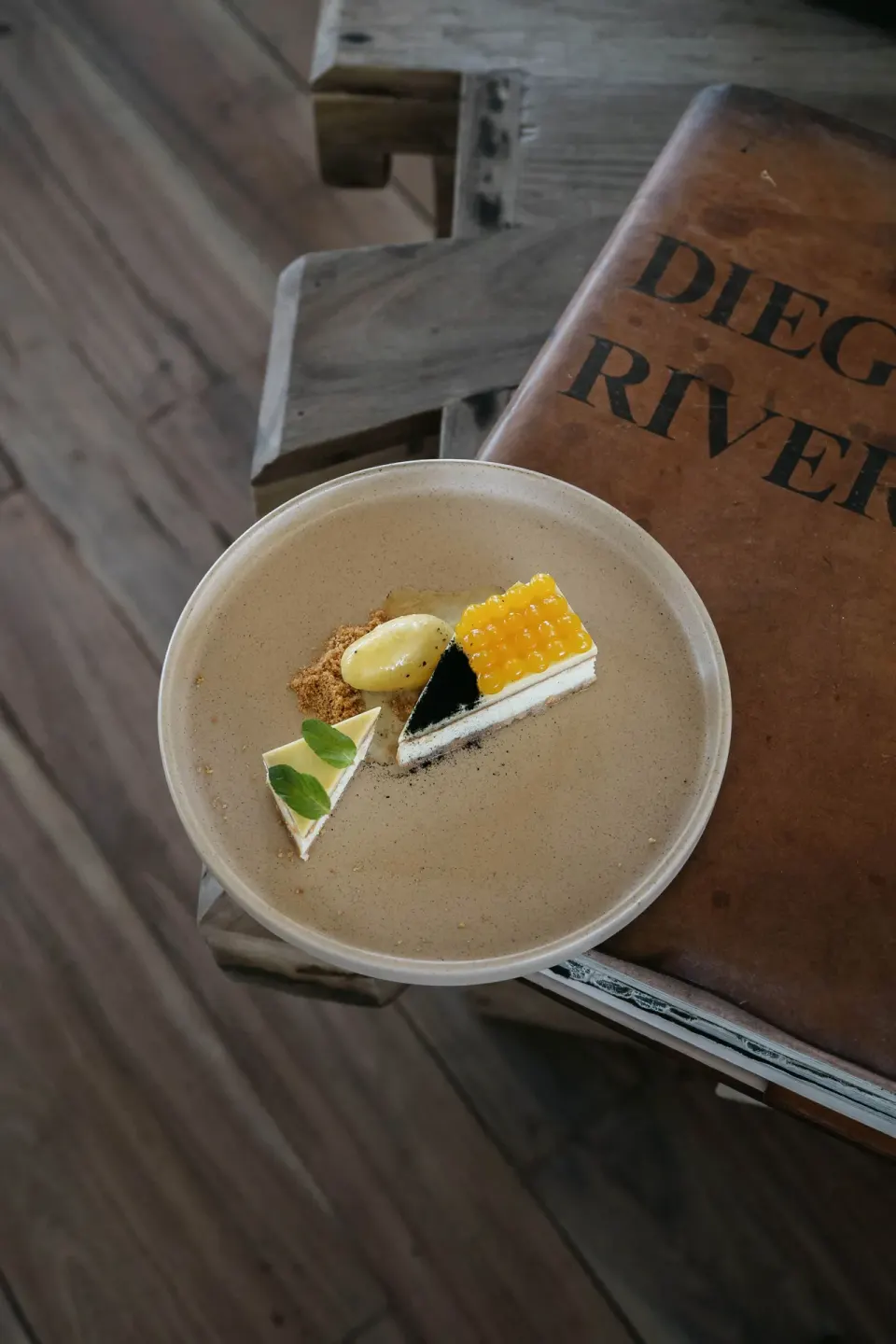 Dessert in a bowl placed beside a large book on a wooden floor at La Valise Tulum