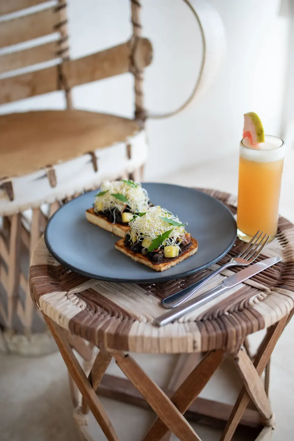 Two pieces of savory toast and a tropical juice on a woven stool at La Valise Tulum