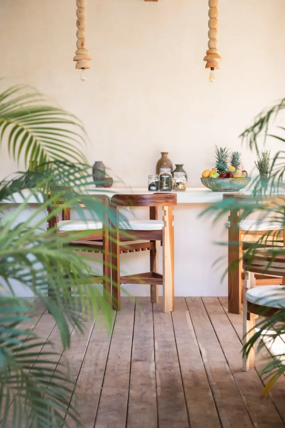 Wooden bar counter and chairs framed by tropical plants at La Valise Tulum