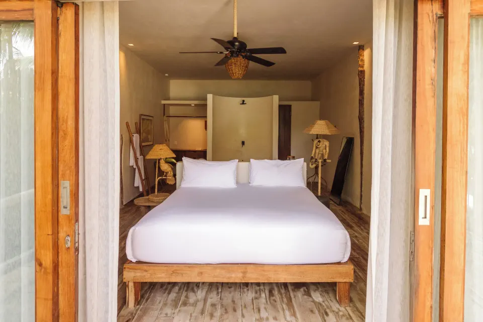 Centered king bed framed by wooden doors and minimal decor at La Valise Tulum beachfront room