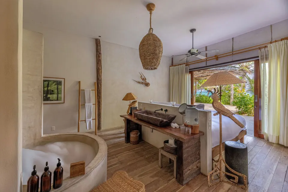 Open-plan room showing bed, washbasin counter, and bathtub with view to the beach at La Valise Tulum