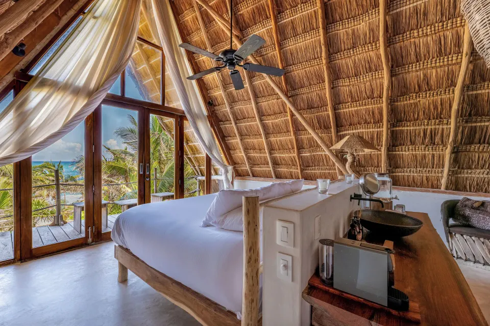 Beachfront Upper Room bed and vanity area under palapa roof with ocean glimpses at La Valise Tulum