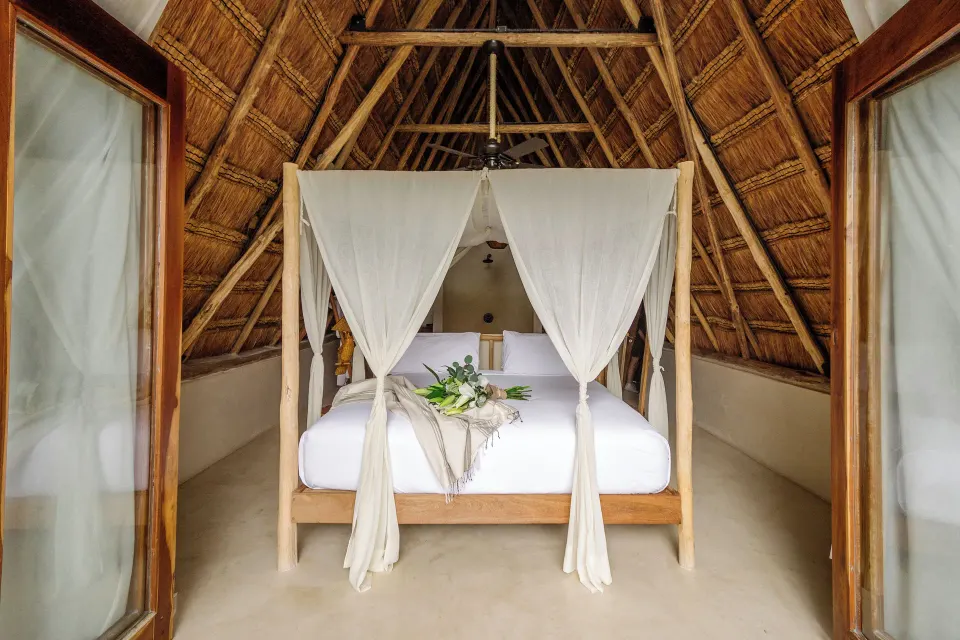 Canopy bed framed by thatched roof and open doors in Beachfront Upper Room at La Valise Tulum