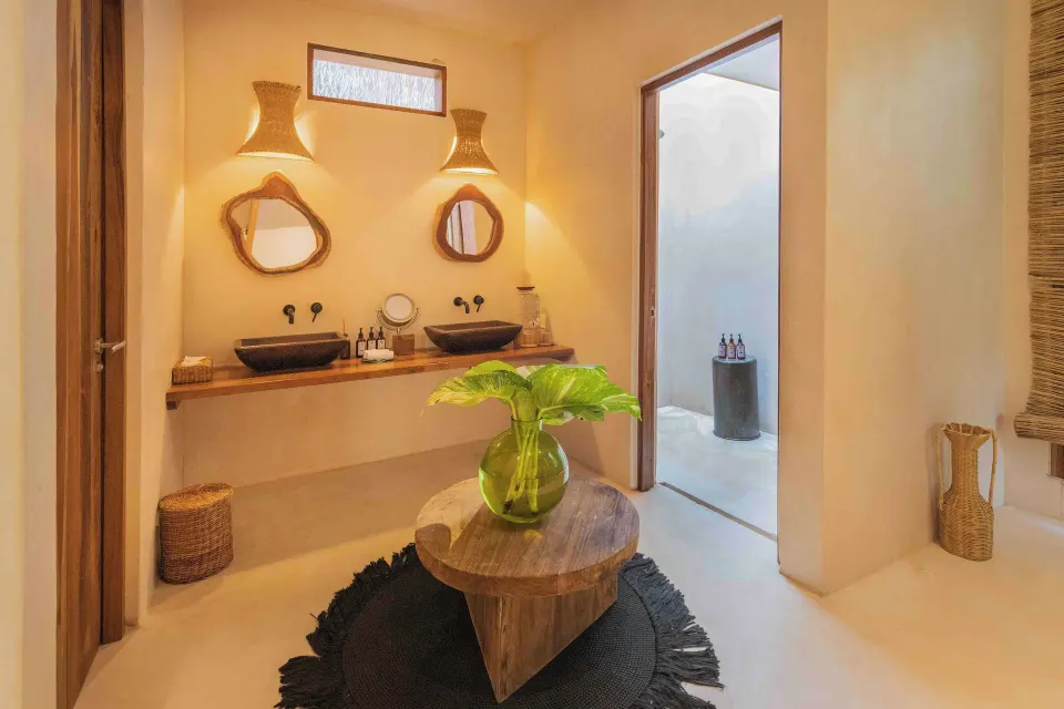 Bathroom with dual sinks, round mirrors and doorway to outdoor shower in Garden Suite Lower at La Valise Tulum
