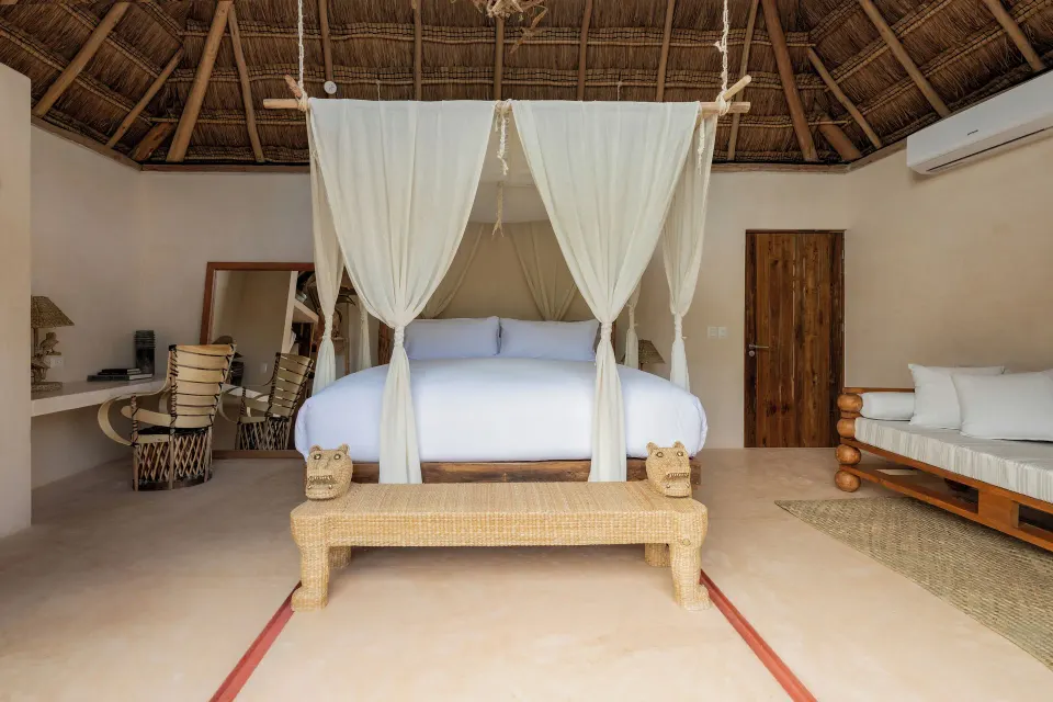 Front view of a canopied bed beneath a thatched roof and seating area at La Valise Tulum