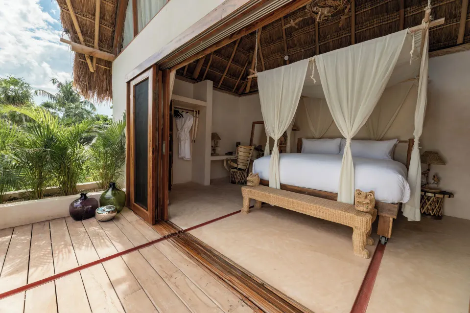 Open-air bedroom with canopied bed and wooden deck framed by palms at La Valise Tulum