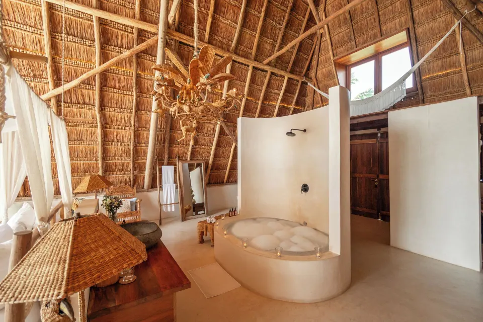Open-plan bathroom in a master suite with a freestanding tub, shower, and chandelier at La Valise Tulum.