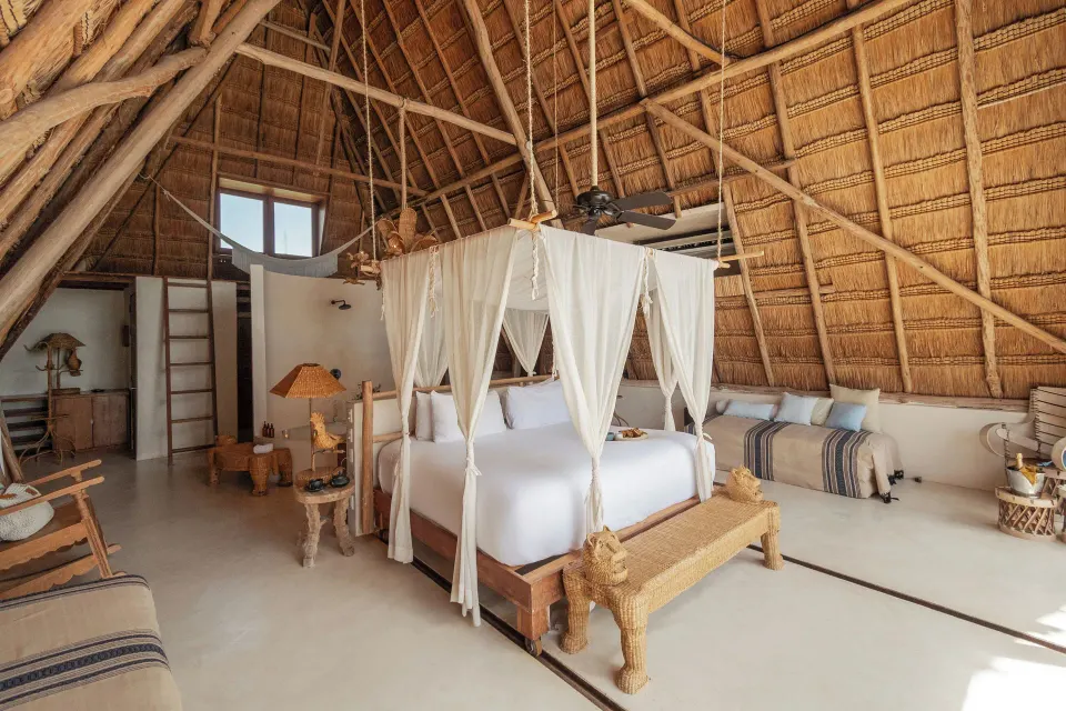 Interior of a master suite with a four-poster bed under a high thatched roof at La Valise Tulum.