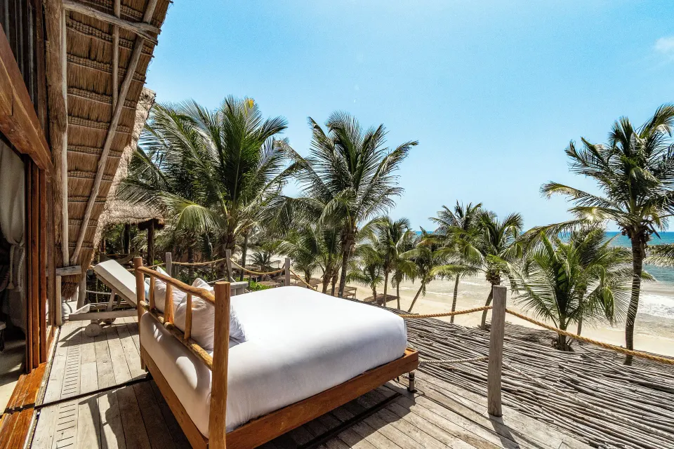 Outdoor daybed on a wooden terrace overlooking palm trees and the beach at La Valise Tulum.