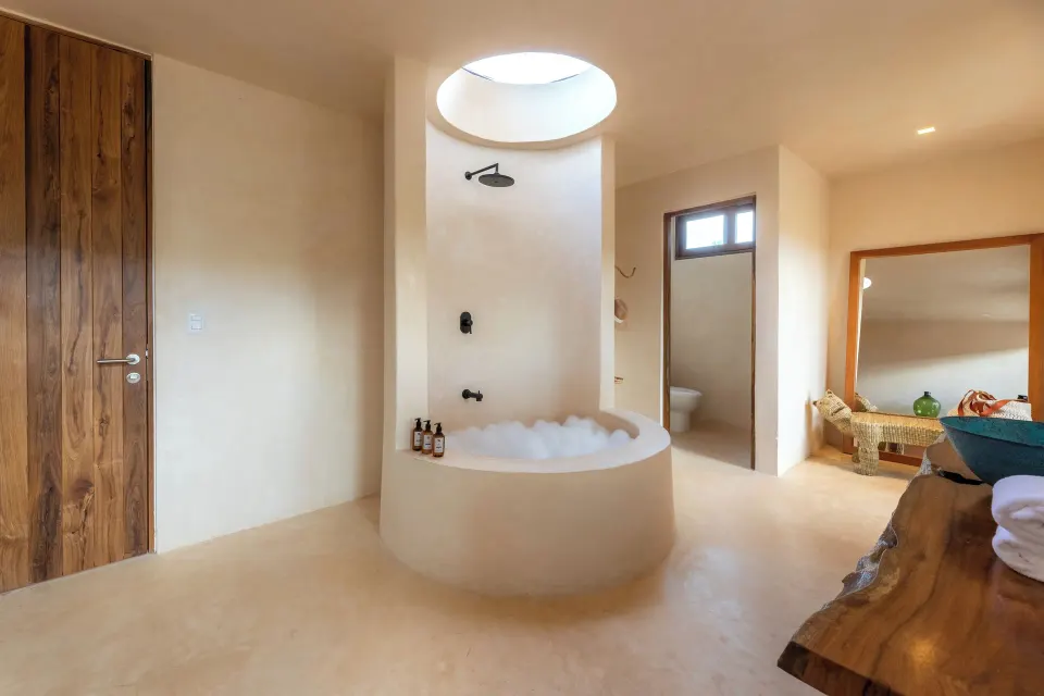 Round soaking tub and open shower in a pale plaster bathroom at La Valise Tulum