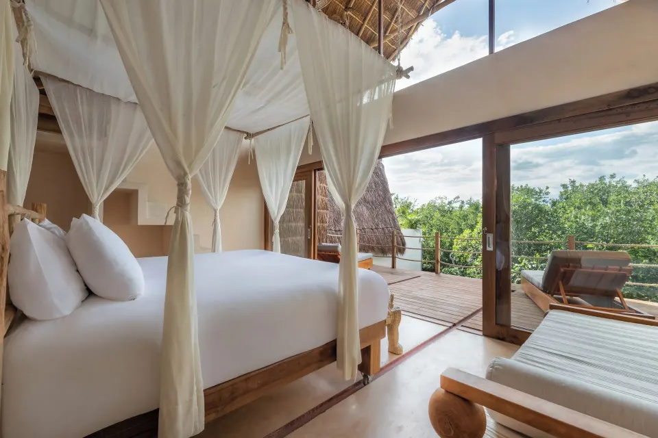 Four‑poster king bed and open sliding doors to a wooden terrace at La Valise Tulum