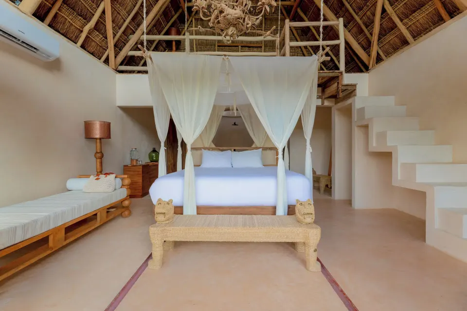 Front view of a canopied king bed and loft stairs inside the Signature Suite Upper at La Valise Tulum