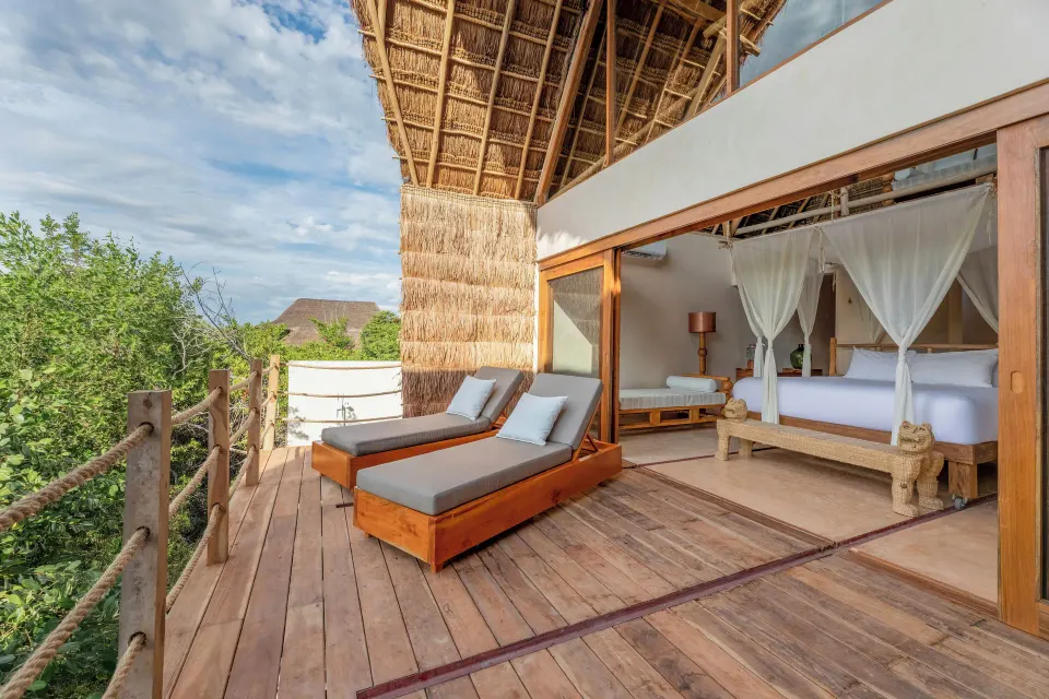 Wooden terrace with two chaise lounges and an open bedroom at La Valise Tulum