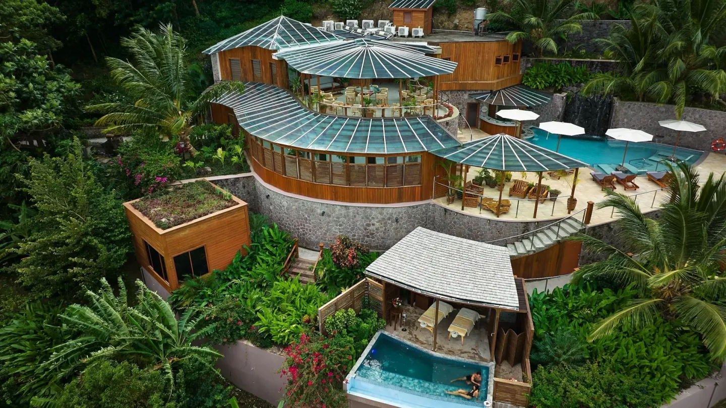 An aerial view of Ladera Resort shows glass-roofed buildings, pools, and tropical gardens.