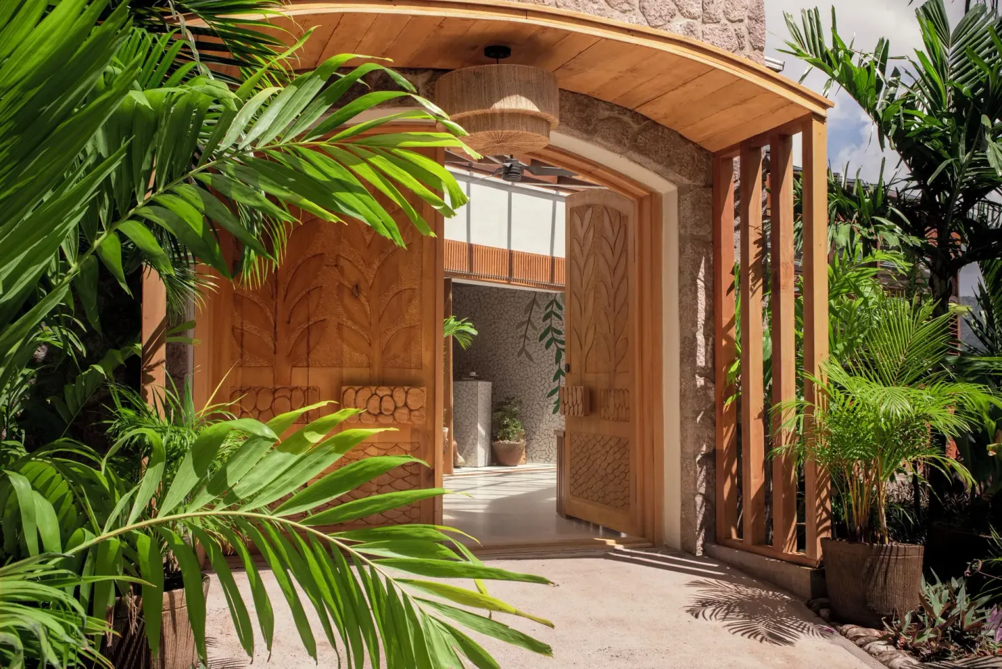 Carved wooden doors open through tropical planting into Ladera Resort.