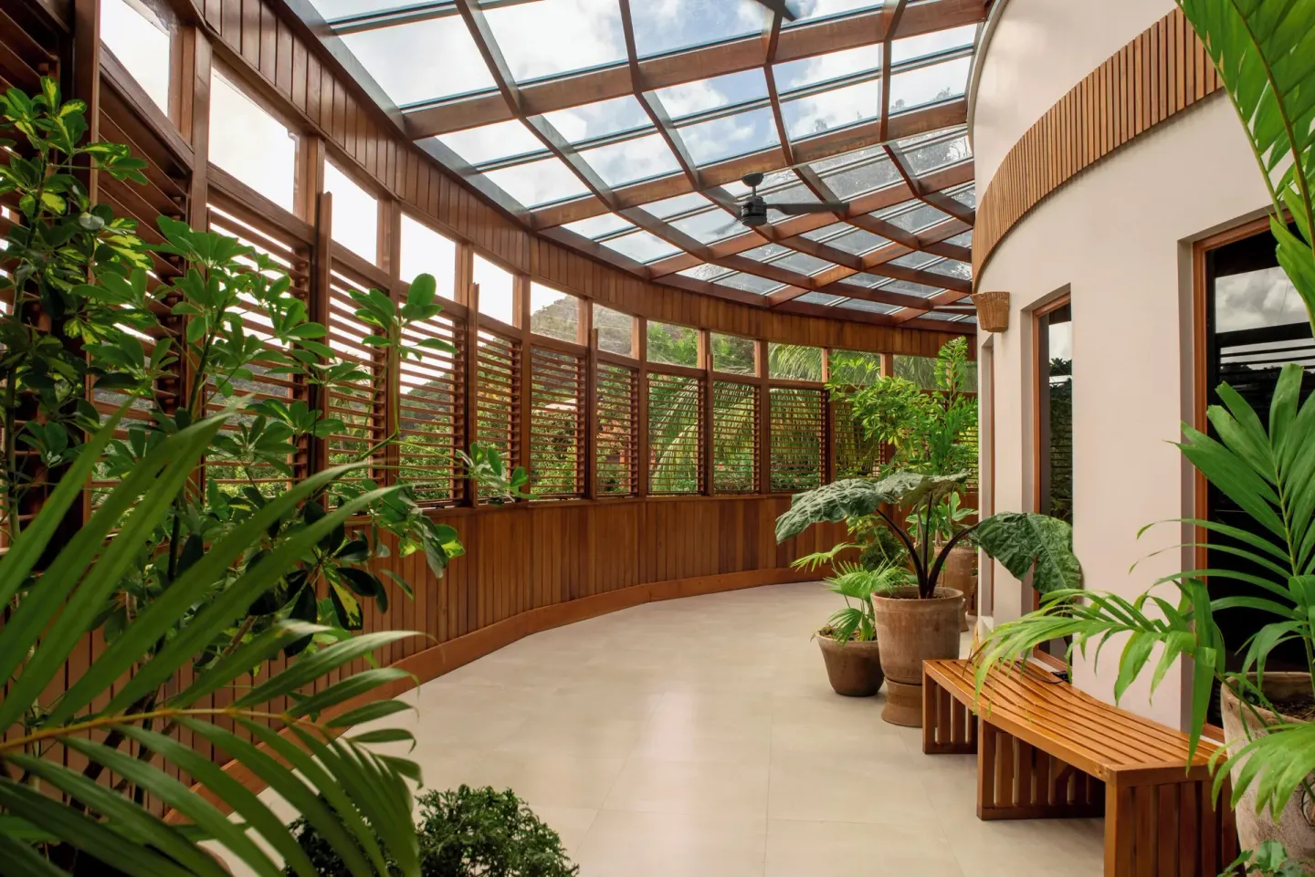A curved indoor walkway with plants, wood shutters, and a glass roof at Ladera Resort.