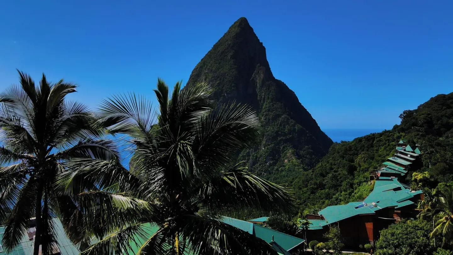 Green-roofed resort buildings and palms below a Piton at Ladera Resort.