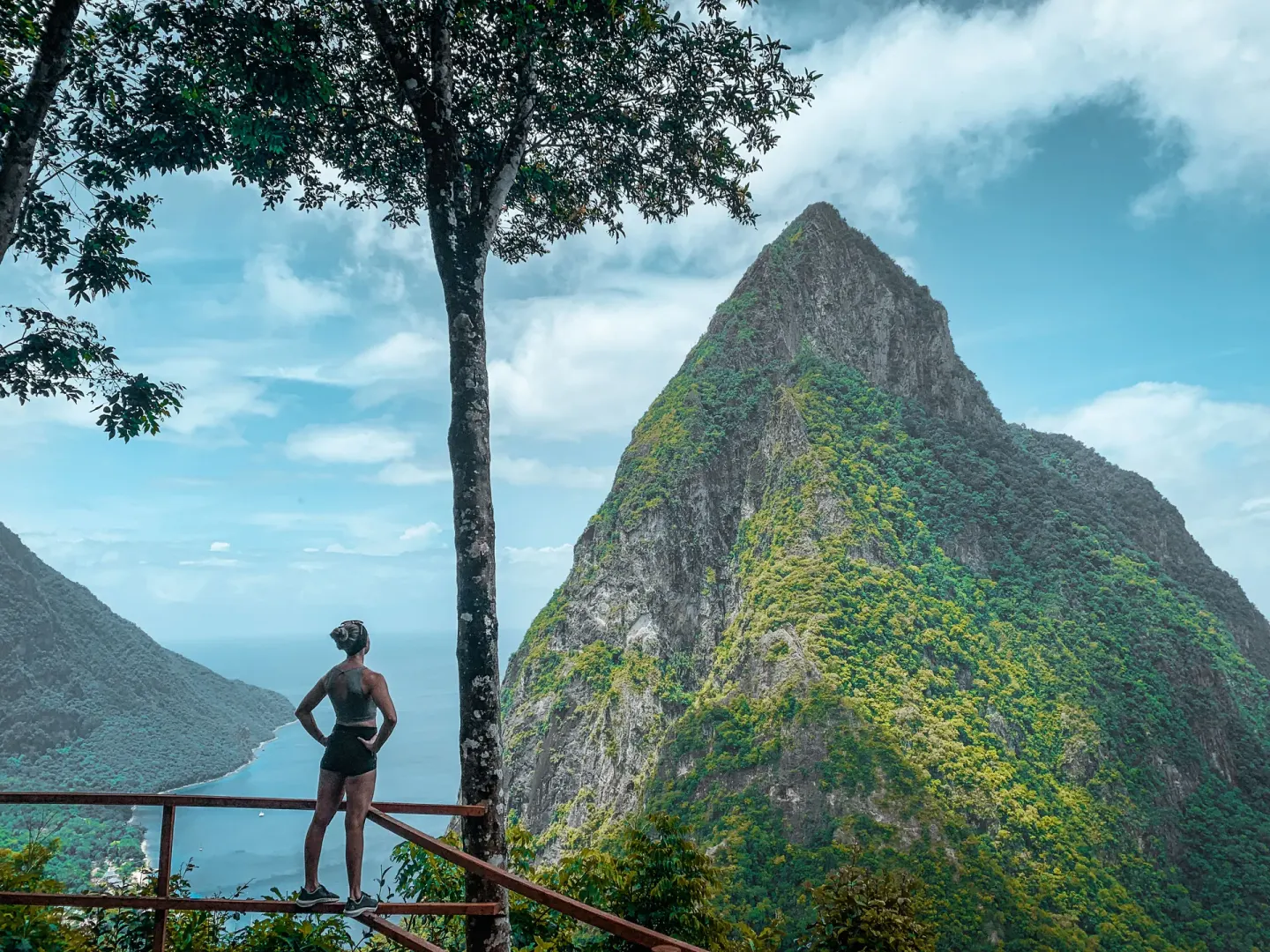 A hiker looks toward a steep green mountain and coastline near Ladera Resort.