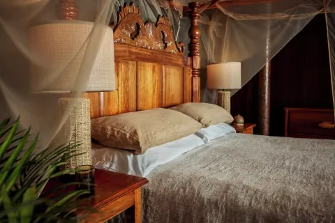 Carved wooden king bed with mosquito netting in the Gros Piton Suite at Ladera Resort.