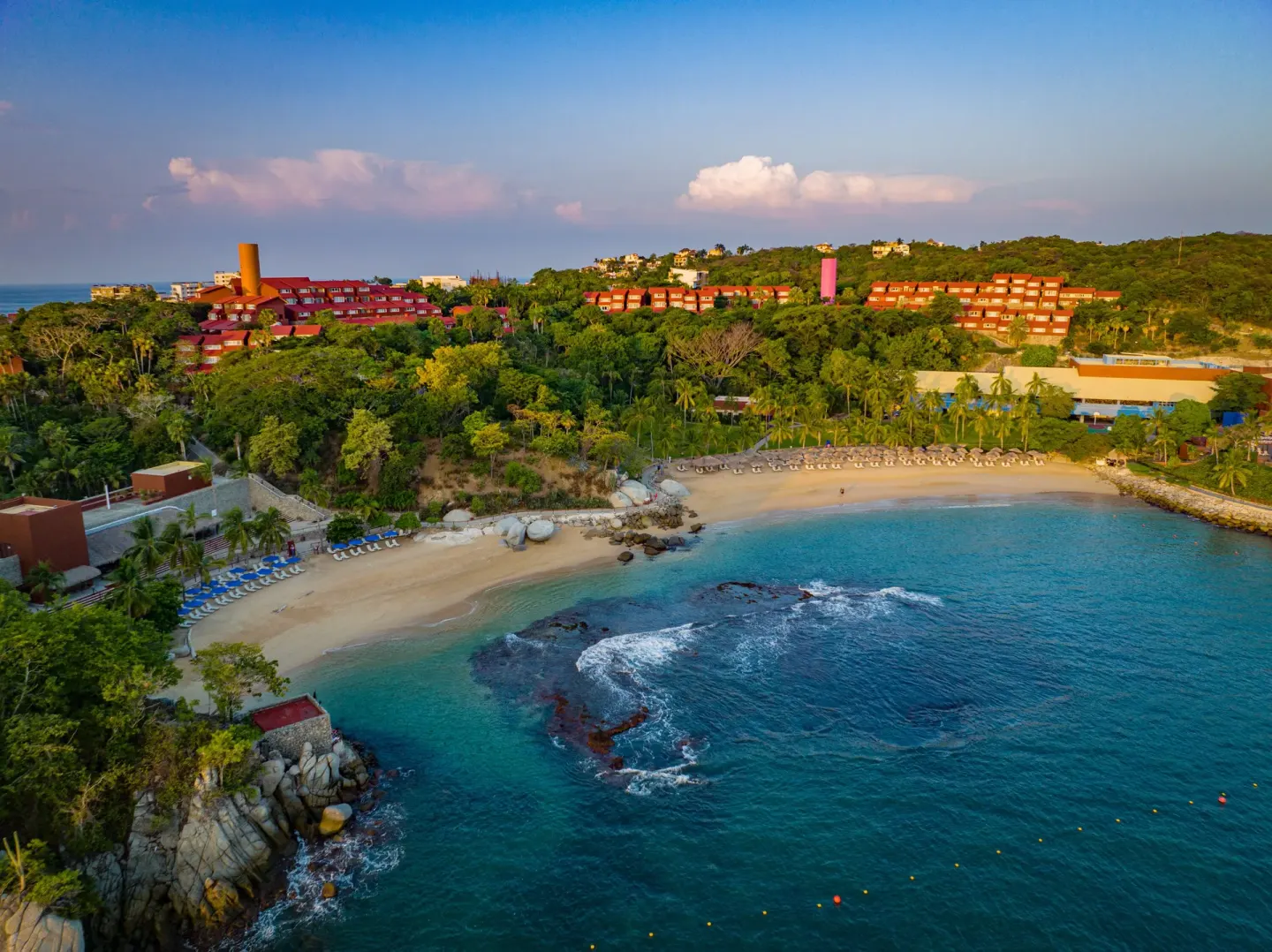Aerial view of the beach, bay, and hillside resort buildings at Las Brisas Huatulco.
