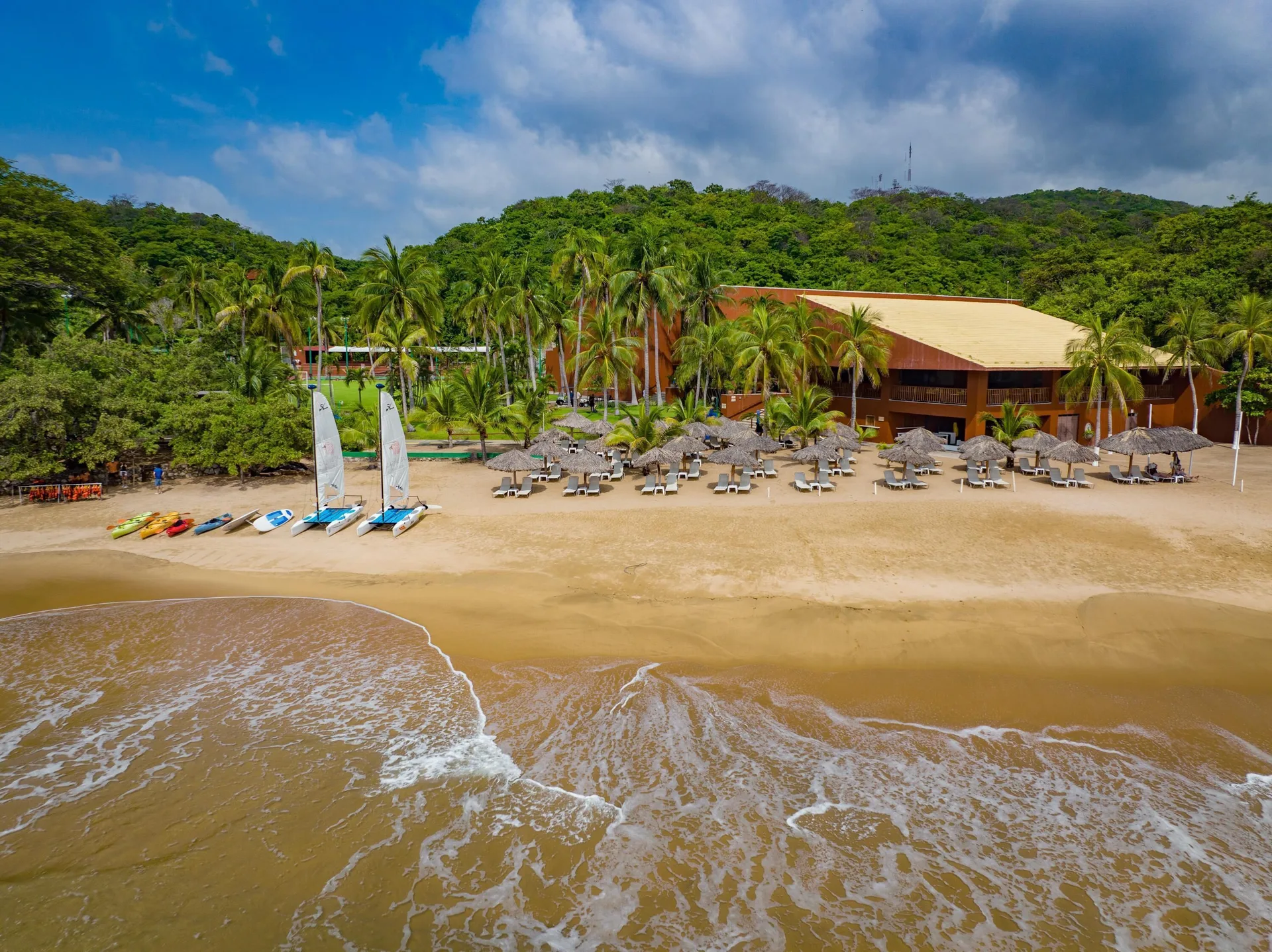 Beach with palapas, loungers, sailboats, and palms at Las Brisas Huatulco.