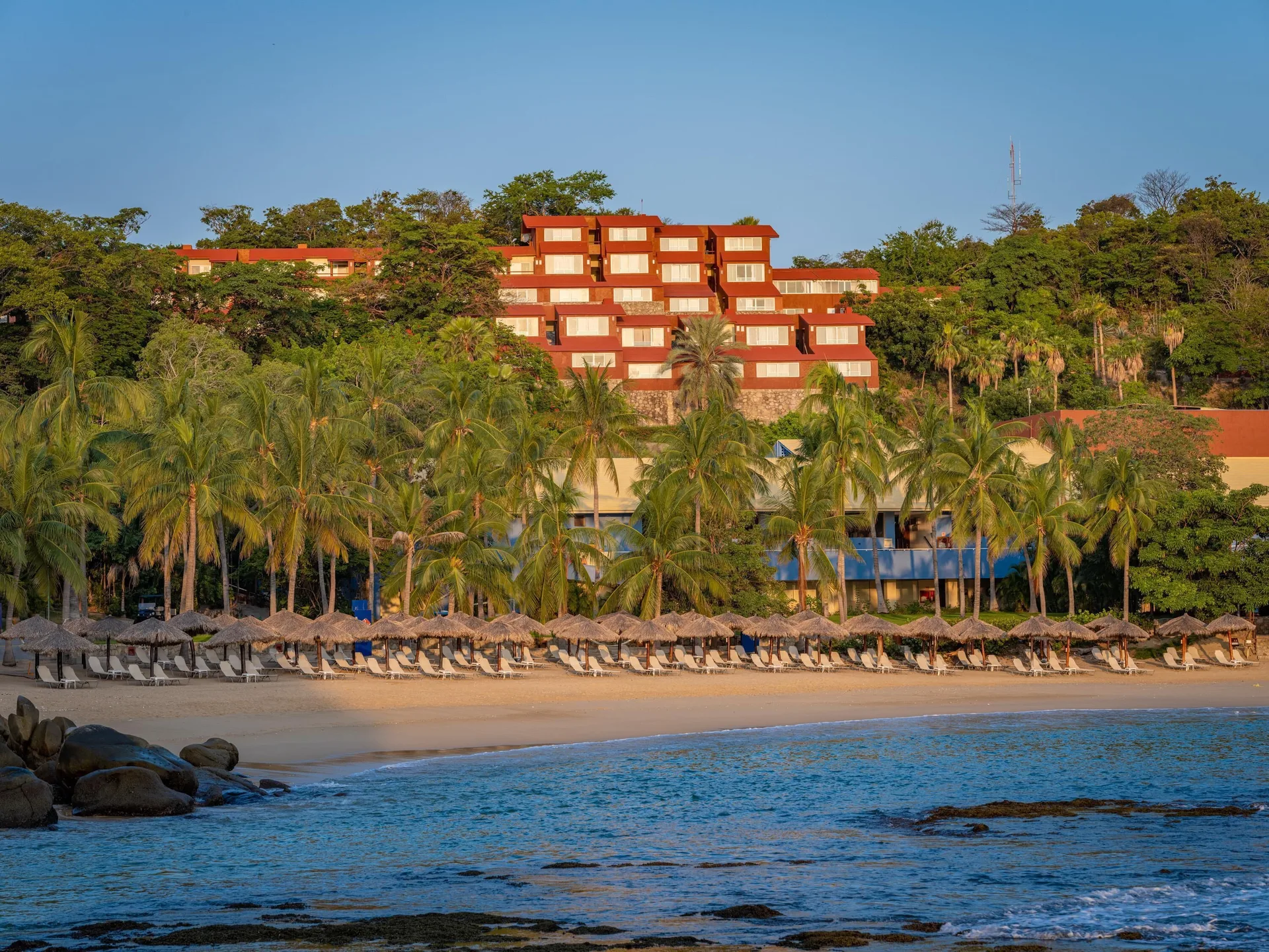 Beachfront palms and hillside lodging buildings at Las Brisas Huatulco.