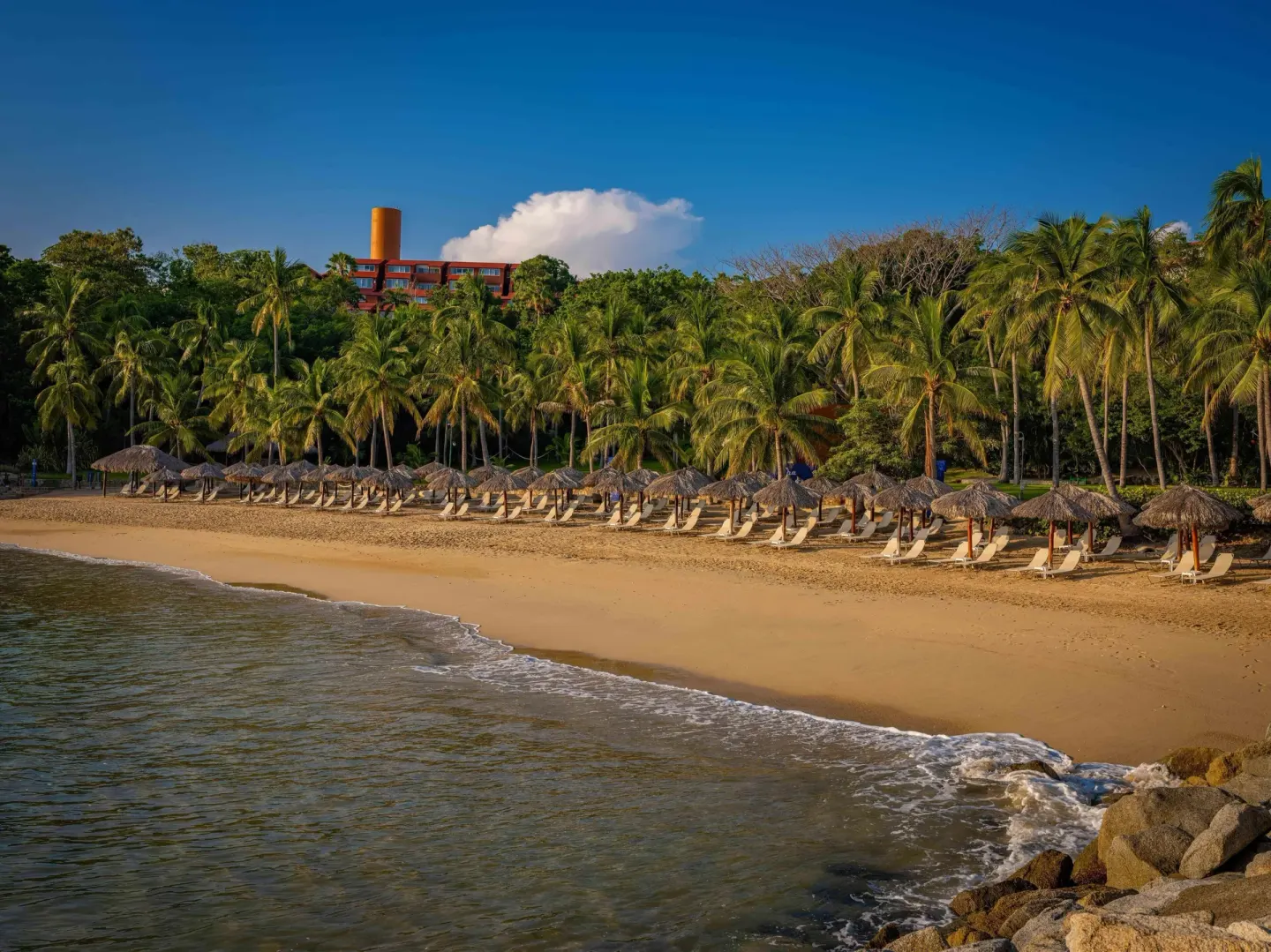 Palm-lined beach with rows of palapas and loungers at Las Brisas Huatulco.