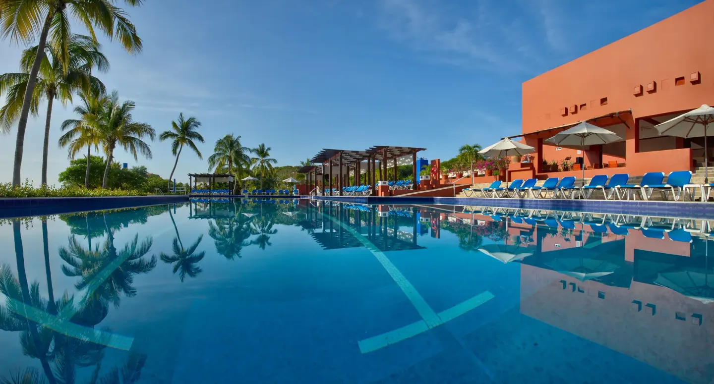 Reflective swimming pool with lounge chairs, umbrellas and palms at Las Brisas Huatulco.