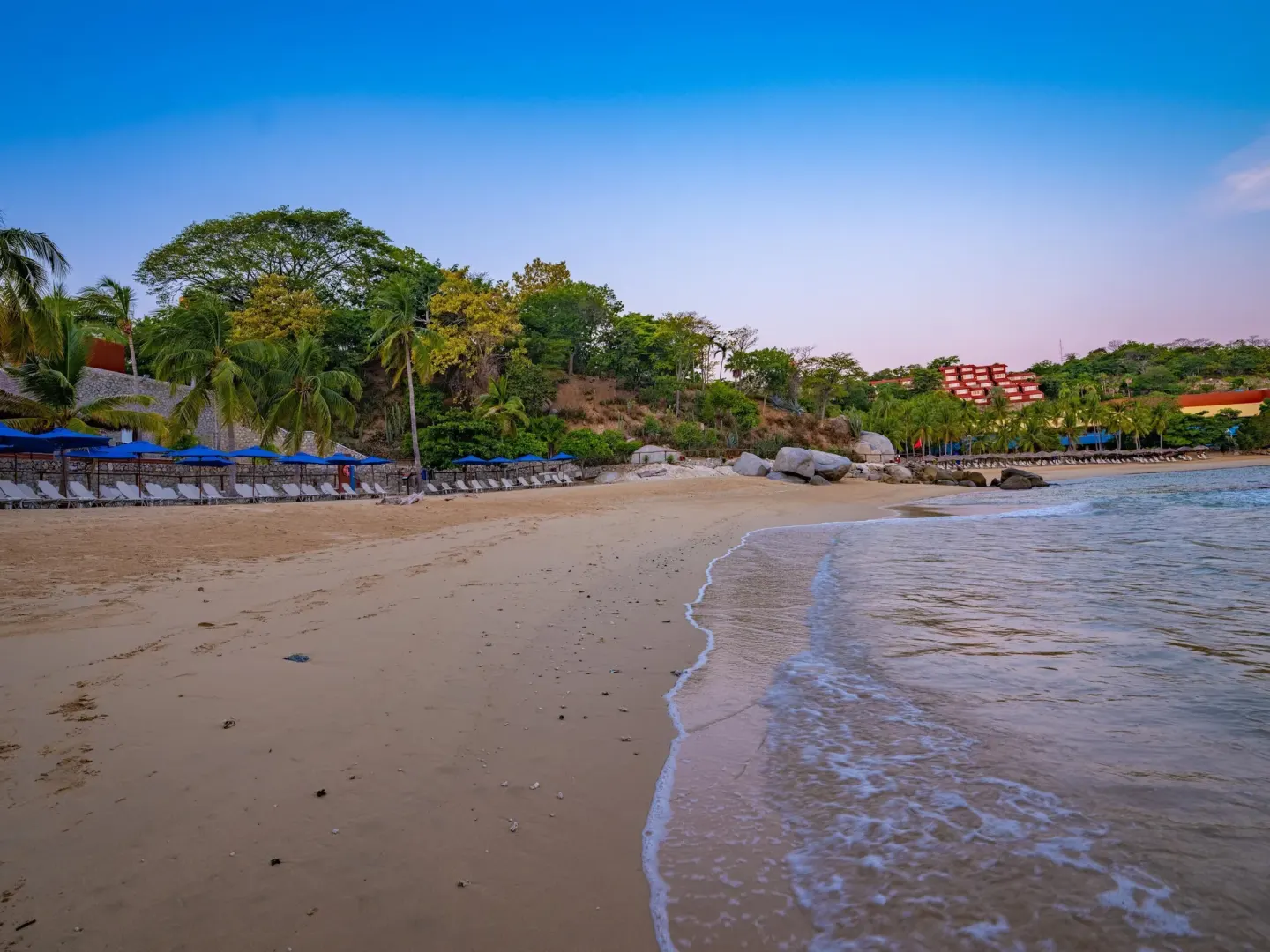 Quiet sandy beach with blue umbrellas and gentle surf at Las Brisas Huatulco.