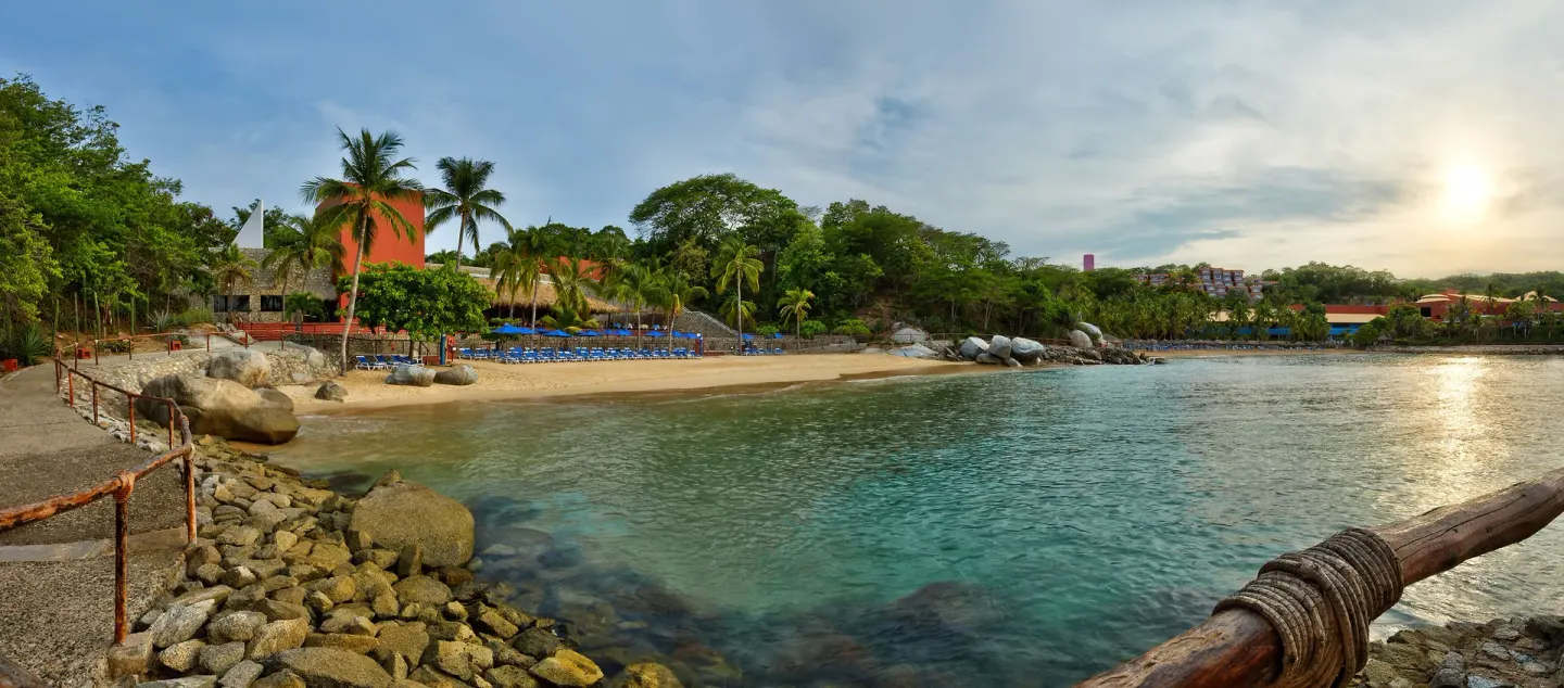 Rocky cove beach with loungers and palm trees at Las Brisas Huatulco.