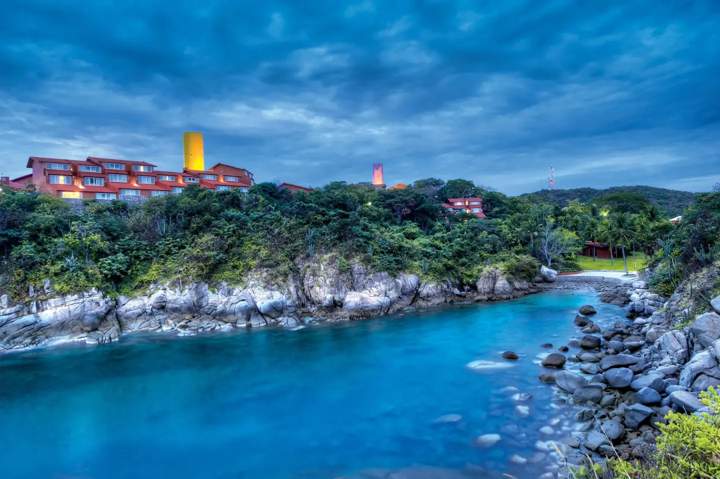 Rocky cove with turquoise water and hillside buildings at Las Brisas Huatulco.