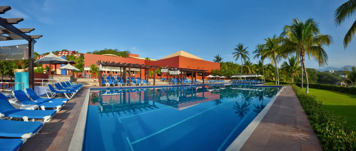 Wide resort pool with blue loungers, pergolas and palm-lined landscaping at Las Brisas Huatulco.