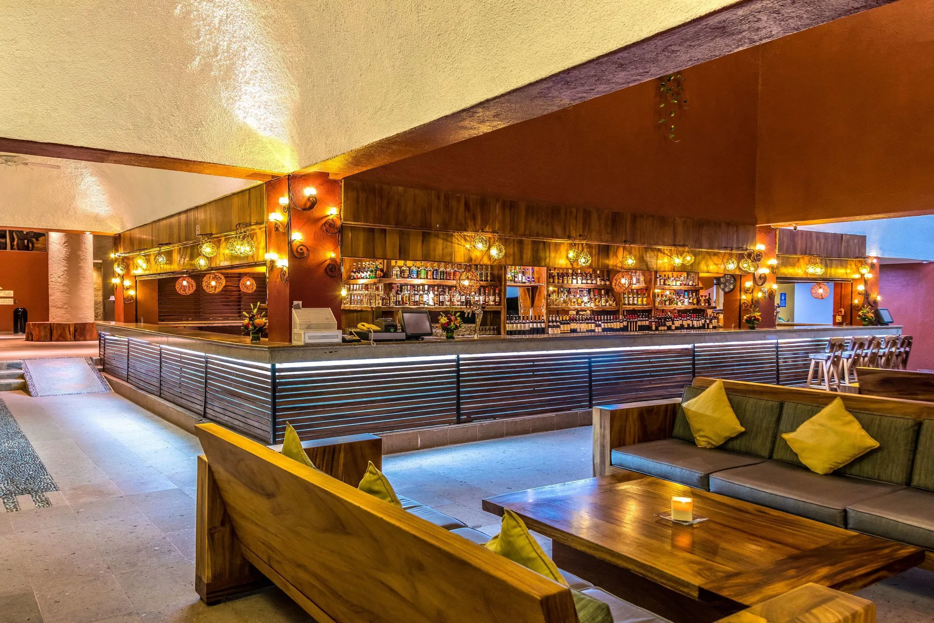 Large lounge bar with wooden seating and illuminated shelves at Las Brisas Huatulco.