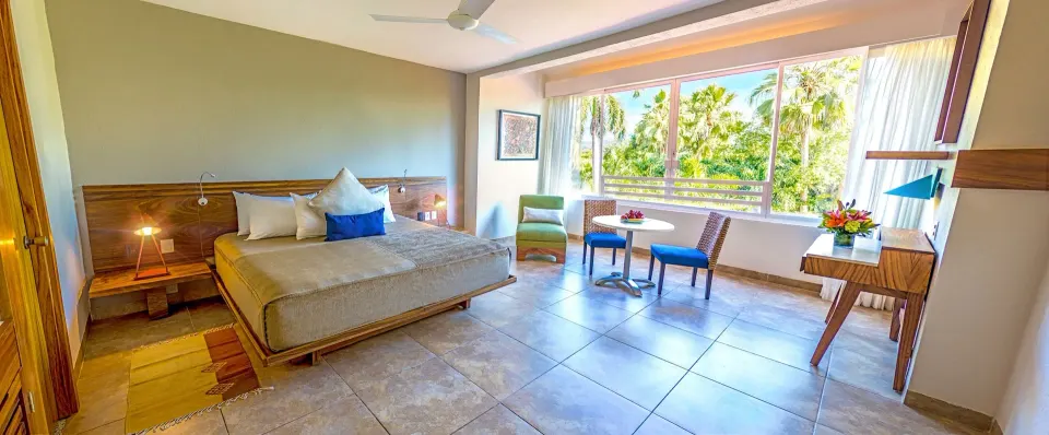 Deluxe Room king bed, desk, and seating area with palm view at Las Brisas Huatulco.