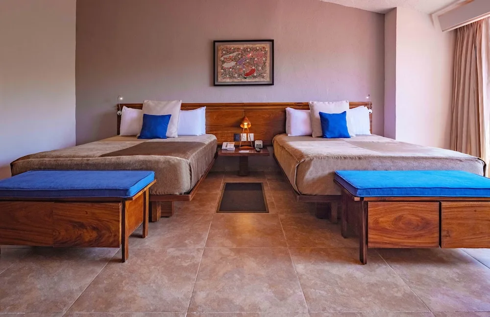 Deluxe room with two beds, wood headboard and blue benches at Las Brisas Huatulco.