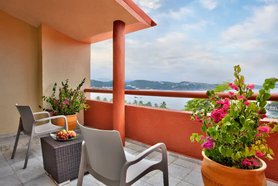 Junior Suite balcony with chairs, flowers, and bay view at Las Brisas Huatulco.